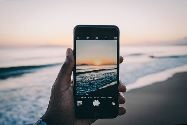 Un usuario hace una foto de la puesta de sol en la playa con su iPhone, Foto 1